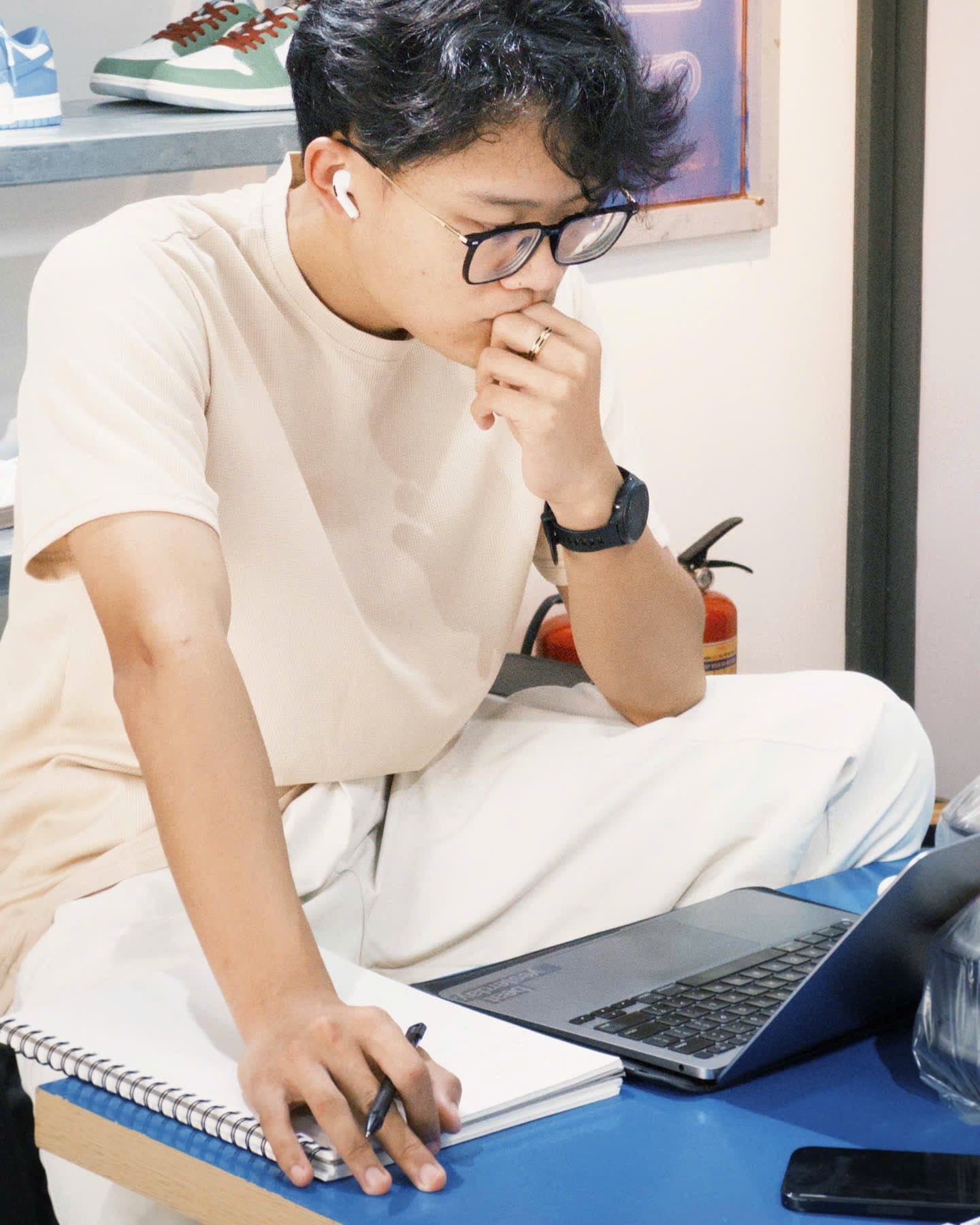 Hồ Lê Thanh Hoàng suy nghĩ bên sổ tay và laptop
